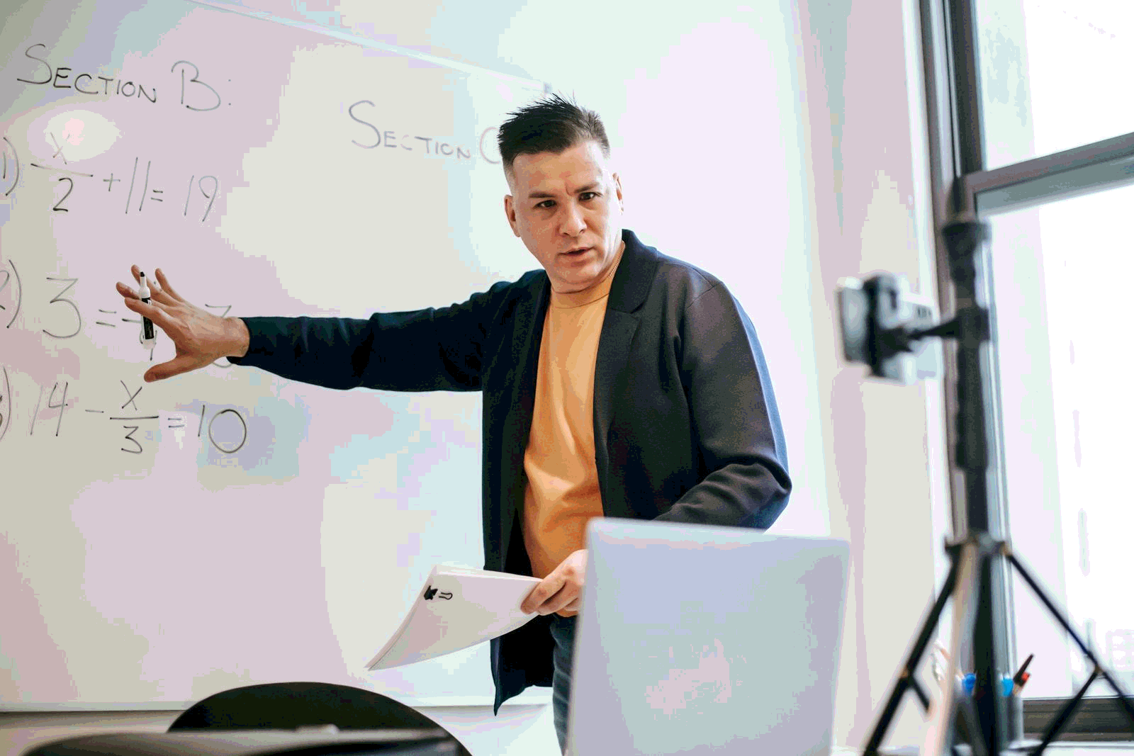 Instructor teaching online with a laptop and whiteboard in a modern classroom