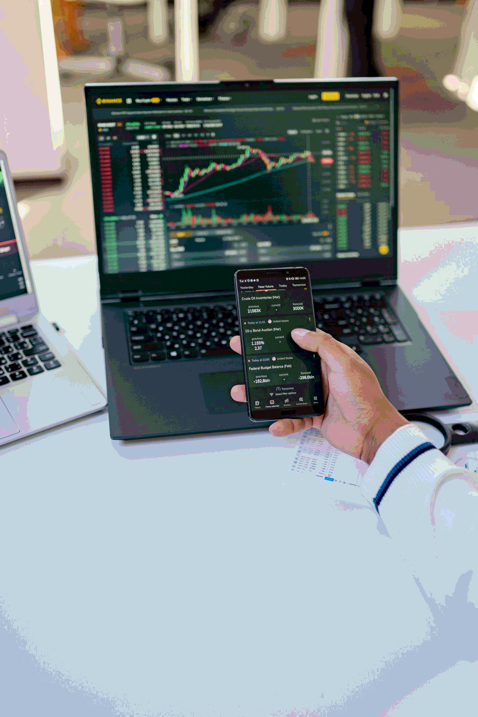 Person analyzing stock market data on a laptop and smartphone at a desk