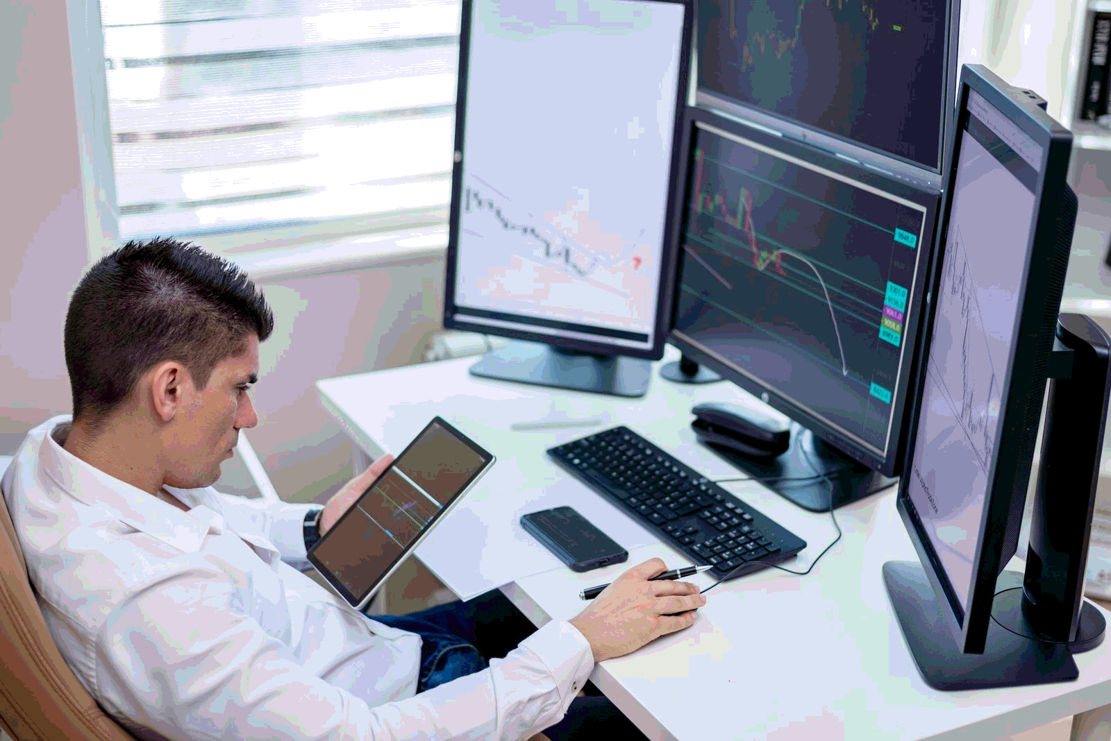 Business professional analyzing financial charts on monitors and tablet in a modern office