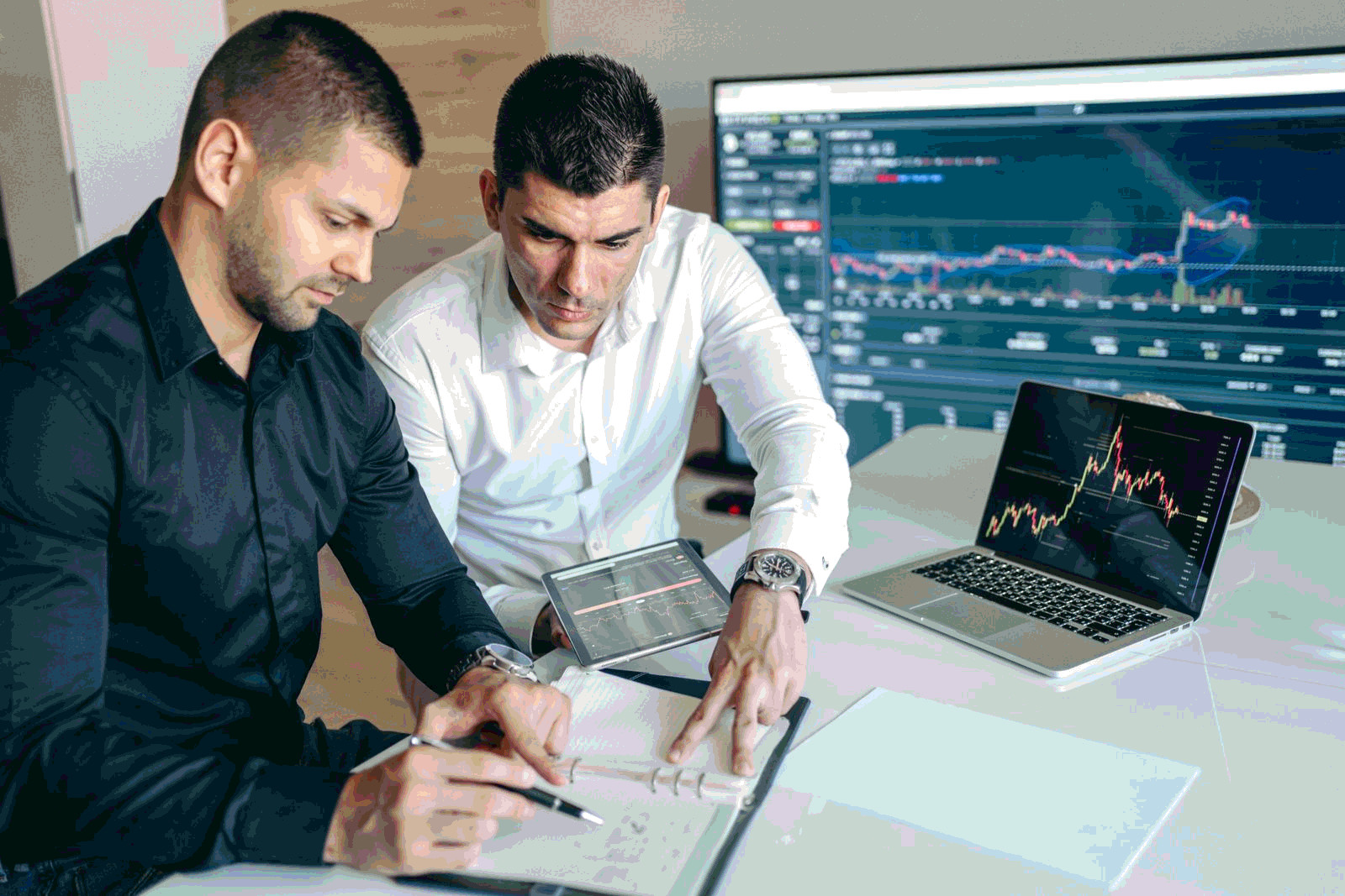 Two risk professionals analyzing financial charts and metrics on laptops and tablets